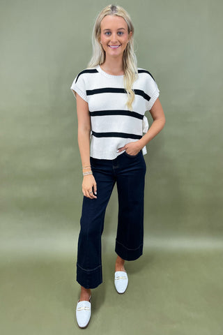 White knit top with black horizontal stripes and side bow detail styled with dark wide leg cropped jeans and white loafers