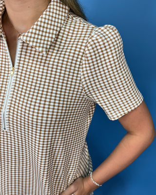 A close-up of a person wearing a brown and white gingham short-sleeve polo shirt with a half-zip neckline