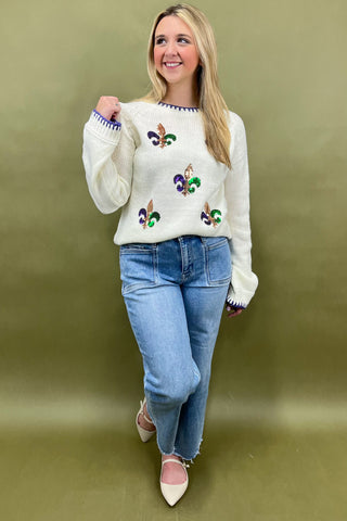 Woman wearing a white sweater with colorful designs and blue jeans on a green background