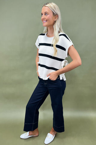 White knit top with black horizontal stripes and side bow detail styled with dark wide leg cropped jeans and white loafers