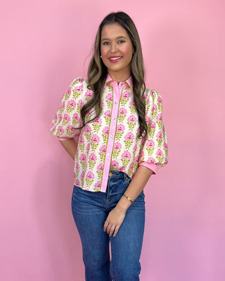 Woman wearing a pink floral blouse with blue jeans against a pink background