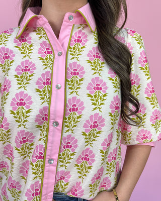 Person wearing a floral patterned shirt with pink and green colors on a pink background
