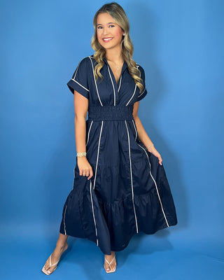 Navy midi dress with crisp white piping, a flattering V-neckline, short sleeves, smocked waist, and tiered flowy skirt.