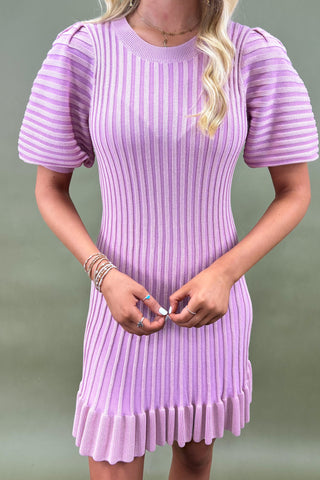 Person wearing a purple ribbed dress against a green background