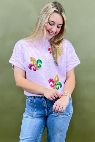 Woman wearing a light purple sweater with colorful designs on a green background