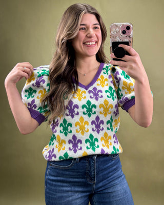 Woman taking a mirror selfie wearing a colorful patterned sweater against a green background