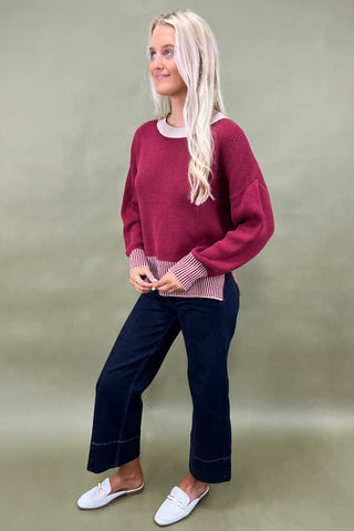 Woman wearing a burgundy sweater, navy pants, and white shoes on a green background