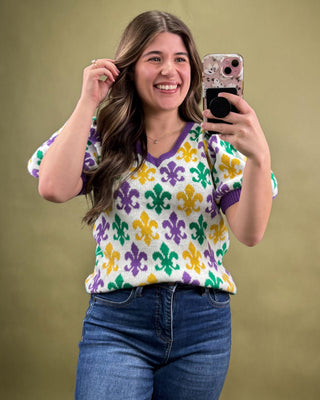 Woman taking a selfie wearing a colorful patterned sweater against a beige background