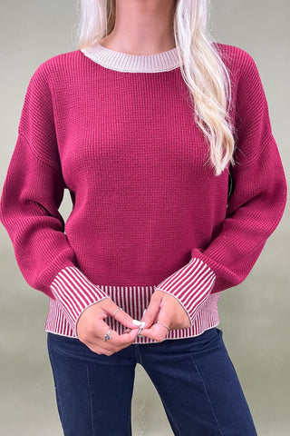 Woman wearing a burgundy sweater and dark blue jeans against a plain background
