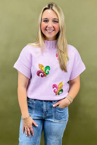 Woman wearing a light purple sweater with colorful designs against a green background