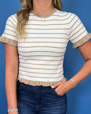 A woman wearing a short-sleeve knit top with beige and white horizontal stripes and ruffled trim