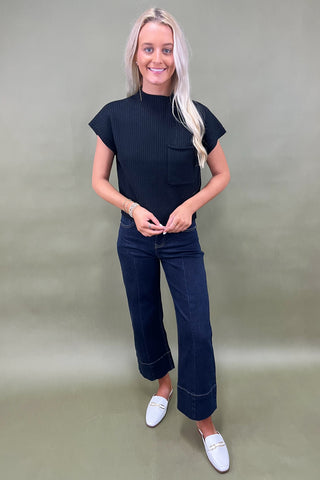 Black ribbed knit top with mock neck and chest pocket styled with dark wide leg cropped jeans and white loafers