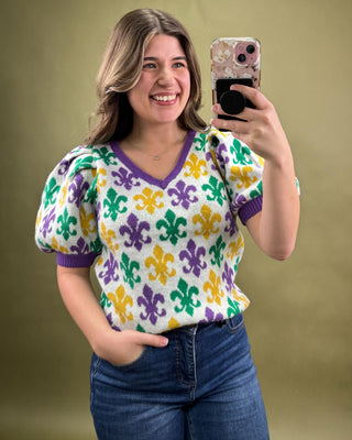 Woman taking a selfie wearing a colorful patterned sweater against a beige background