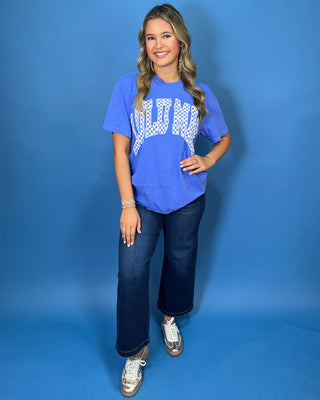 Woman modeling a blue graphic T-shirt with white checkered lettering and dark wash jeans.