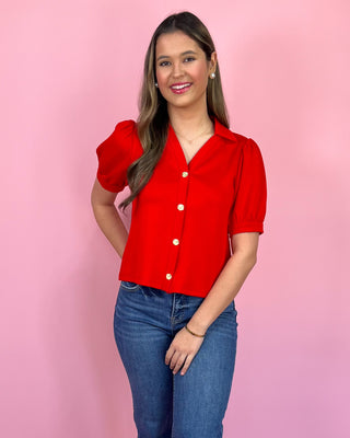Woman wearing a red blouse with puff sleeves against a pink background