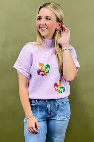 Woman wearing a light purple sweater with colorful designs against a green background