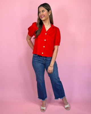 Woman wearing a red blouse and blue jeans against a pink background