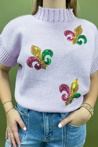 Person wearing a light purple sweater with colorful floral patterns on a green background