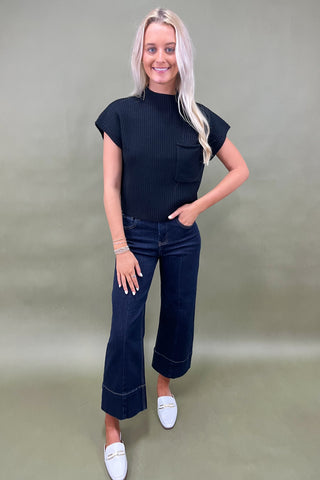 Black ribbed knit top with mock neck and chest pocket styled with dark wide leg cropped jeans and white loafers