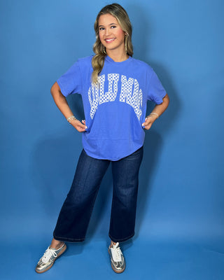 Woman modeling a blue graphic T-shirt with white checkered lettering and dark wash jeans.