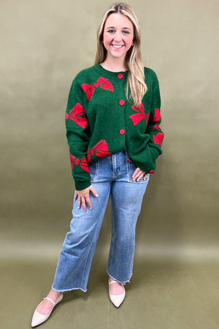 Woman wearing a green sweater with red bow patterns against a beige background