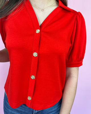 Red blouse with gold buttons worn by a person on a light purple background