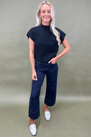 Black ribbed knit top with mock neck and chest pocket styled with dark wide leg cropped jeans and white loafers