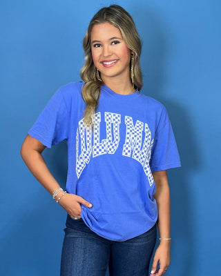 Woman modeling a blue graphic T-shirt with white checkered lettering and dark wash jeans.