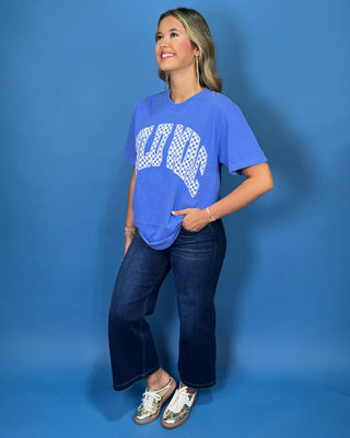 Woman modeling a blue graphic T-shirt with white checkered lettering and dark wash jeans.