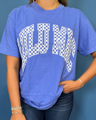 Woman modeling a blue graphic T-shirt with white checkered lettering and dark wash jeans.