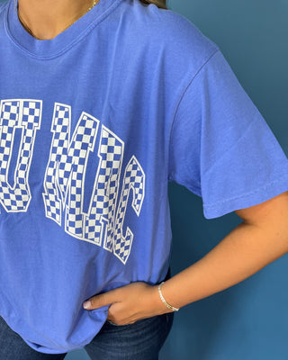 Woman modeling a blue graphic T-shirt with white checkered lettering and dark wash jeans.