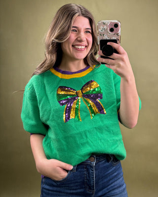 Person wearing a green sweater with a colorful bow design, taking a selfie.