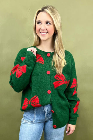 Woman wearing a green sweater with red bow patterns against a beige background
