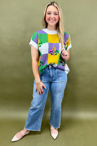 Woman wearing a colorful patterned shirt and blue jeans against a green background