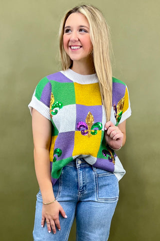 Woman wearing a colorful patchwork sweater with bead embellishments against a green background