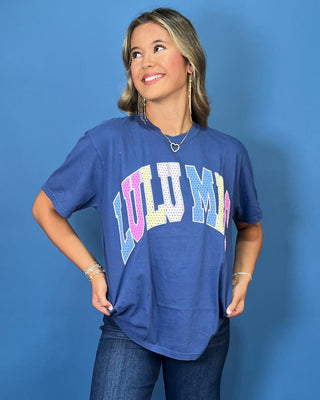 Woman modeling a navy graphic T-shirt with colorful varsity lettering, dark wash wide leg jeans, and sneakers.