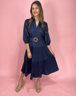 Woman wearing a navy blue dress with a belt on a pink background