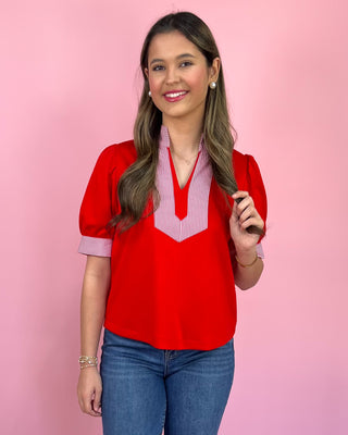 Woman wearing a red blouse with a pink and white striped collar against a pink background
