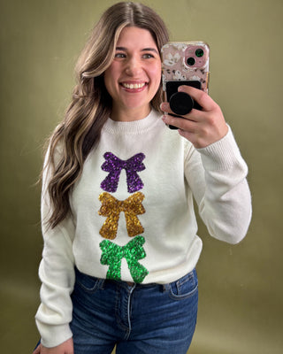 Person wearing a white sweater with colorful bows and taking a selfie against a green background