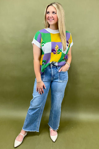 Woman wearing a colorful sweater with a pattern and blue jeans against a green background