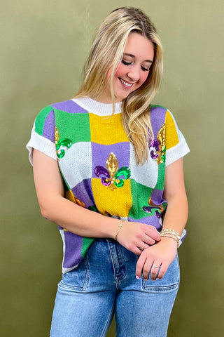 Woman wearing a colorful Mardi Gras-themed sweater against a green background