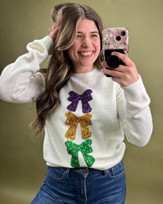 Woman wearing a white sweater with colorful bows, taking a mirror selfie.
