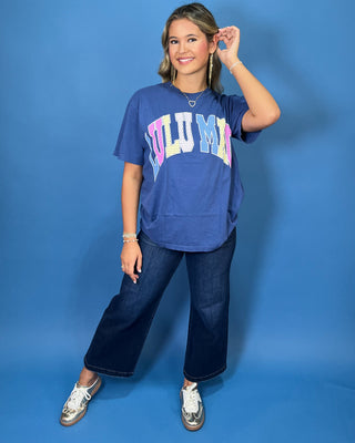 Woman modeling a navy graphic T-shirt with colorful varsity lettering, dark wash wide leg jeans, and sneakers.