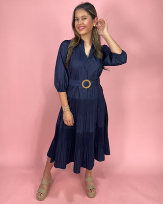 Woman wearing a navy dress with a gold belt against a pink background