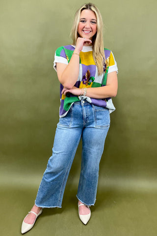 Woman wearing a colorful patterned shirt and blue jeans against a green background