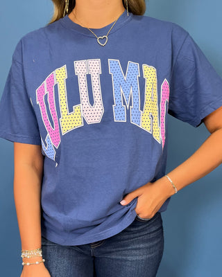 Woman modeling a navy graphic T-shirt with colorful varsity lettering, dark wash wide leg jeans, and sneakers.