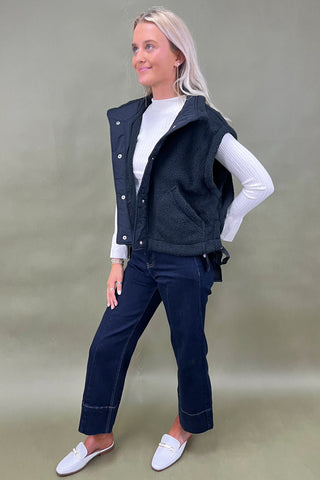 Black sherpa zip vest layered over white ribbed long sleeve top styled with dark wide leg cropped jeans and white loafers.