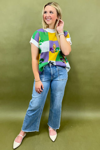Woman wearing a colorful patchwork shirt and blue jeans against a green background