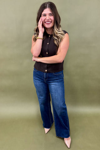 Woman wearing a black sleeveless top and blue jeans against a green background