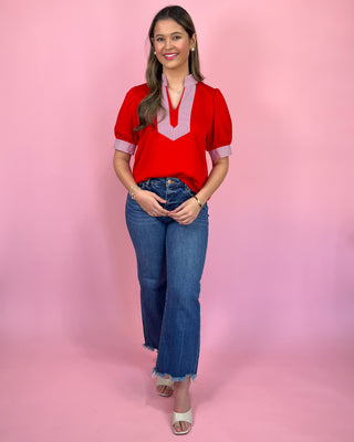 Woman wearing a red blouse and blue jeans against a pink background